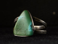 thumbnail of Angled view of a sterling silver ring featuring a large, polished green triangular turquoise stone with natural matrix lines, set against a dark background.