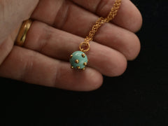thumbnail of Vintage turquoise pendant studded with gold beads, hanging on chain against hand.