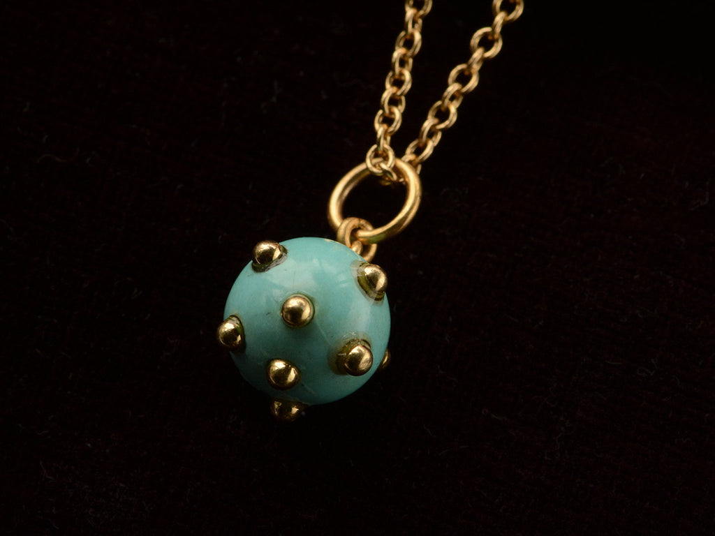 Vintage turquoise pendant studded with gold beads, hanging on chain against black background.