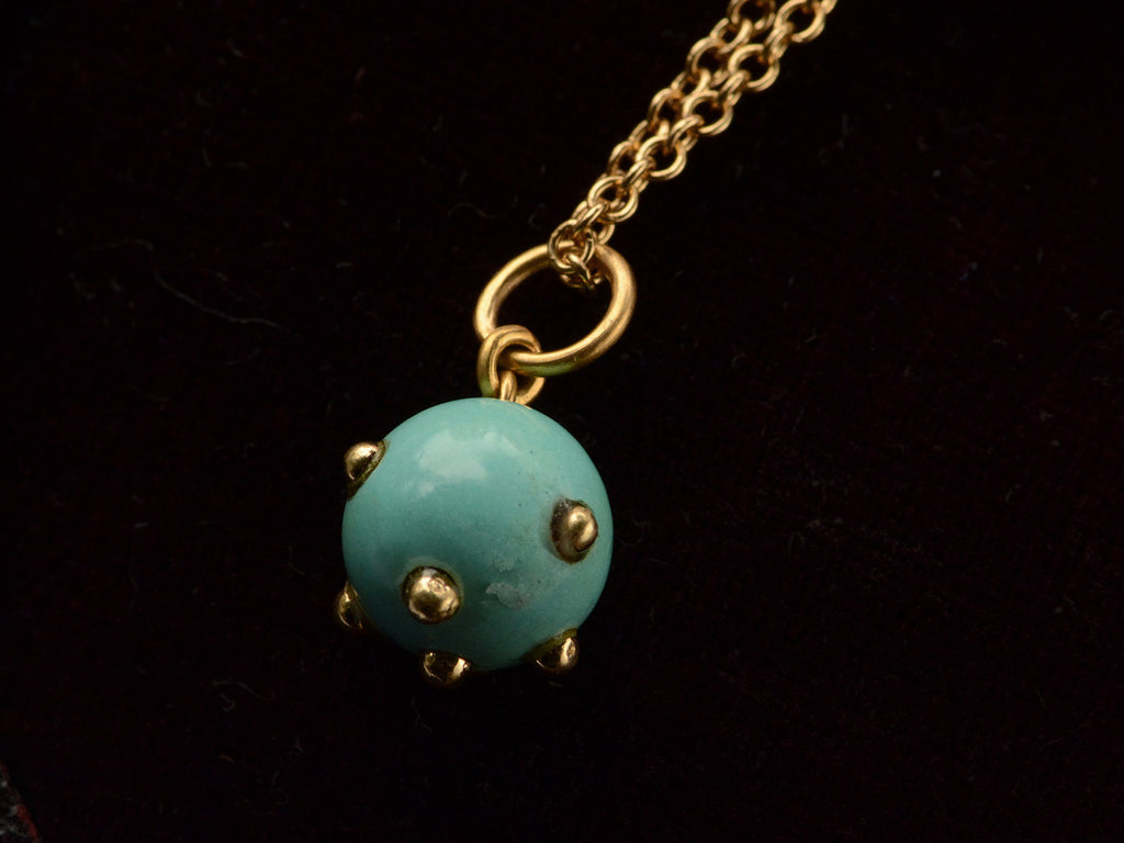 Reverse side of vintage turquoise pendant studded with gold beads, hanging on chain against black background.