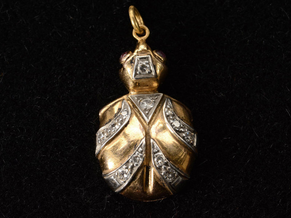 Vintage turtle shaped pendant in white and yellow gold with diamond and ruby details. shown on black background.