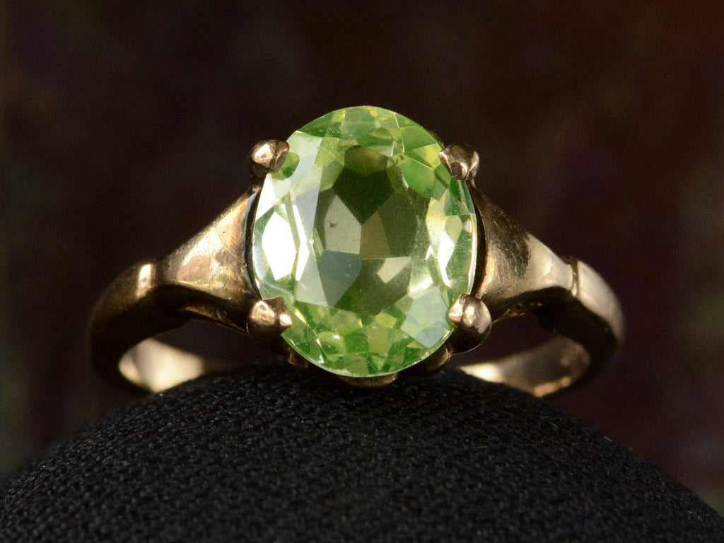 Front of Art Deco ring with oval pale green stone set in rosy-yellow gold, shown on dark background.