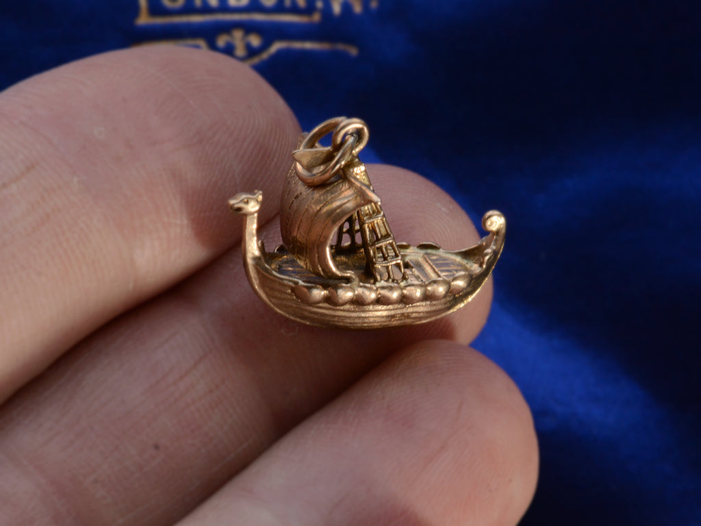 A yellow gold c1960 Viking Ship Charm, shown hand for scale