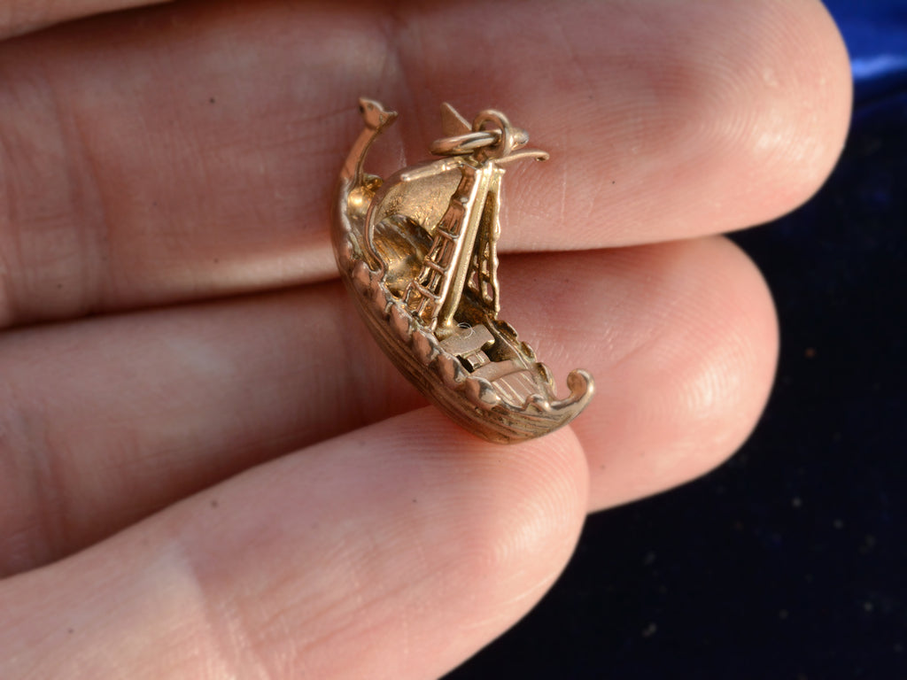 An angled view of a yellow gold c1960 Viking Ship Charm, shown on hand for scale.