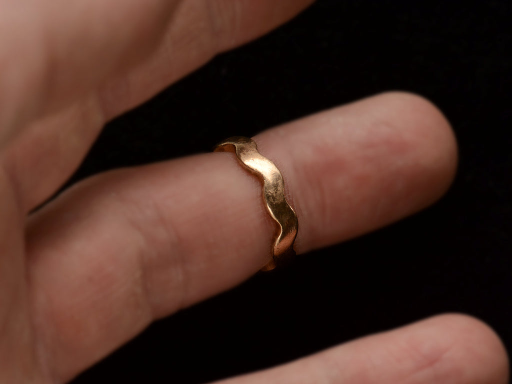 A gold ring with a wave-form design, on a finger