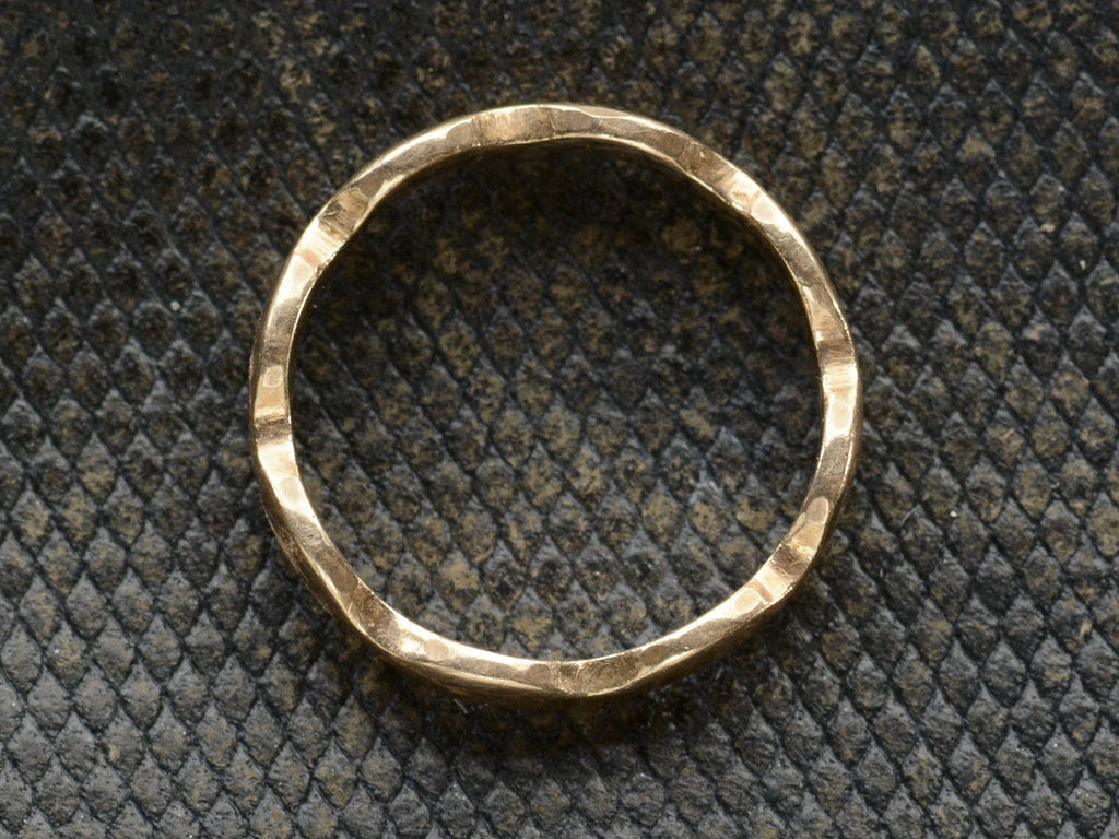 Side profile of a gold ring with a wave-form design, on a dark background.