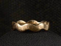 thumbnail of Front view of a gold ring with a wave-form design, on dark background.