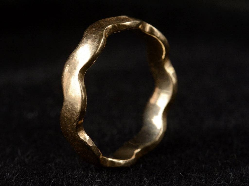Angled view of a gold ring with a wave-form design, on dark background.