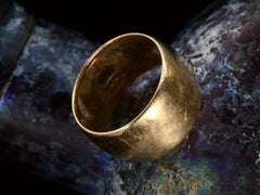thumbnail of Angled view of a wide patinated antique rosy-yellow gold wedding band, on dark background.