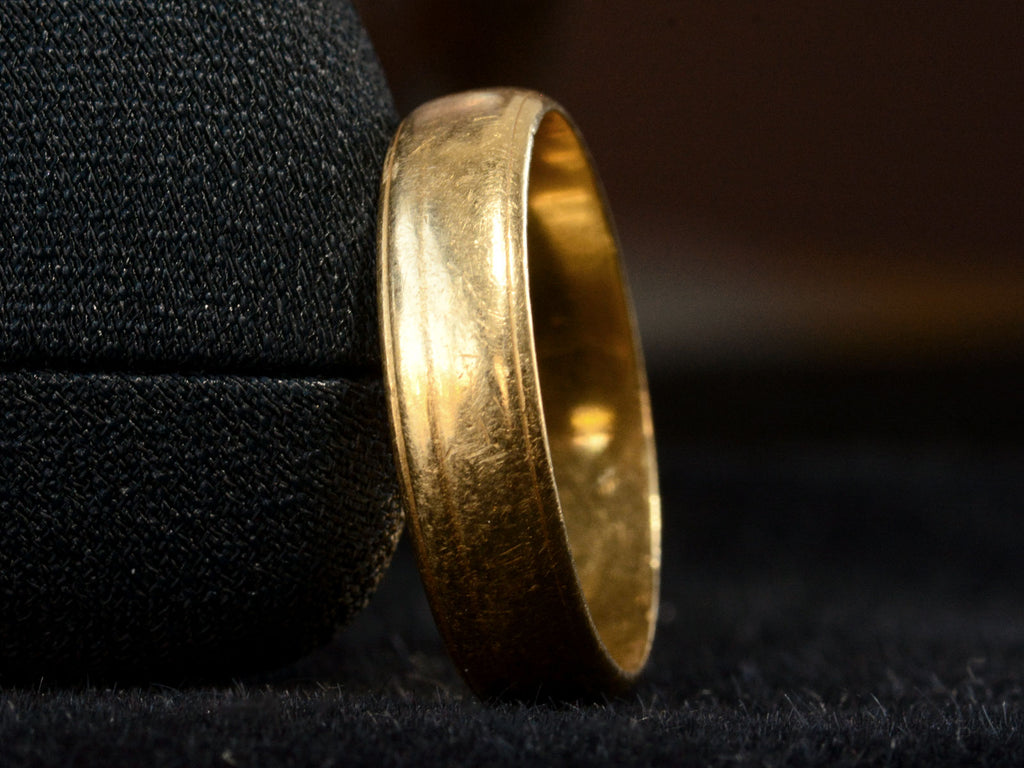 Detail of c1920 Wide 18K yellow gold wedding band with edge detailing. Shown on dark background.