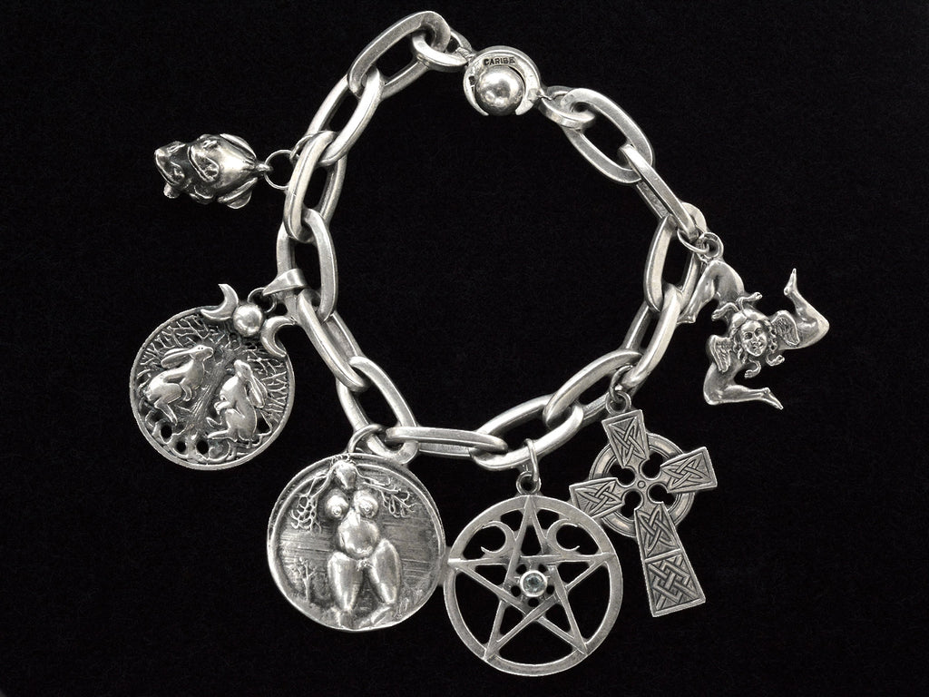 A vintage sterling silver charm bracelet with charms depicting mating frogs, a pair of rabbits perched beneath a tree under crescent moons, a nude woman, a pentagram, a Celtic cross, and the Sicilian Trinacria. On black background.