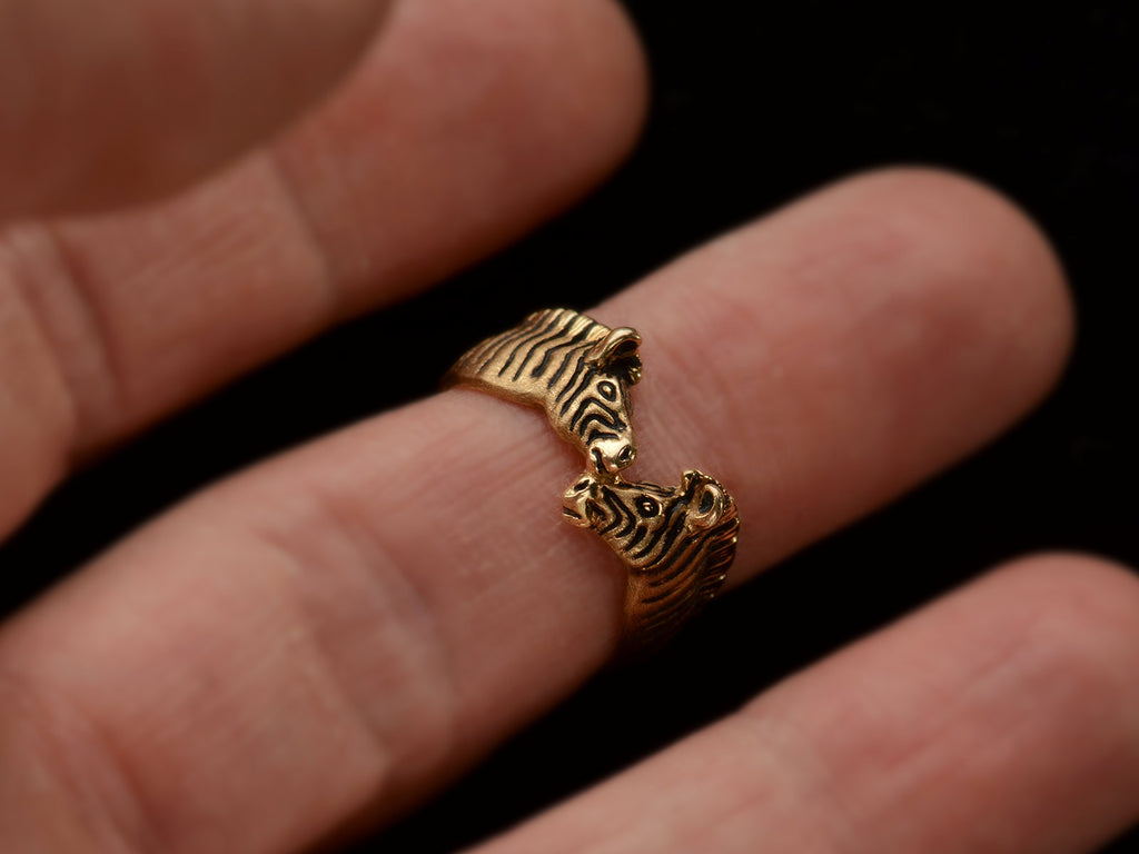 A two-headed zebra ring in 14K with black details, shown on finger.