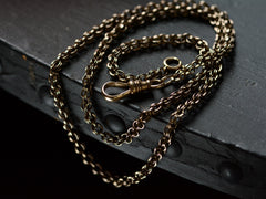 A sturdy Victorian-era gold chain with an unusual link, and a dog clip for attaching a pendant, in addition to a ring clasp that was likely added later. In 14K rosy-yellow gold with a blackened patina. Dates to c1880. Measures 19.5 inches.